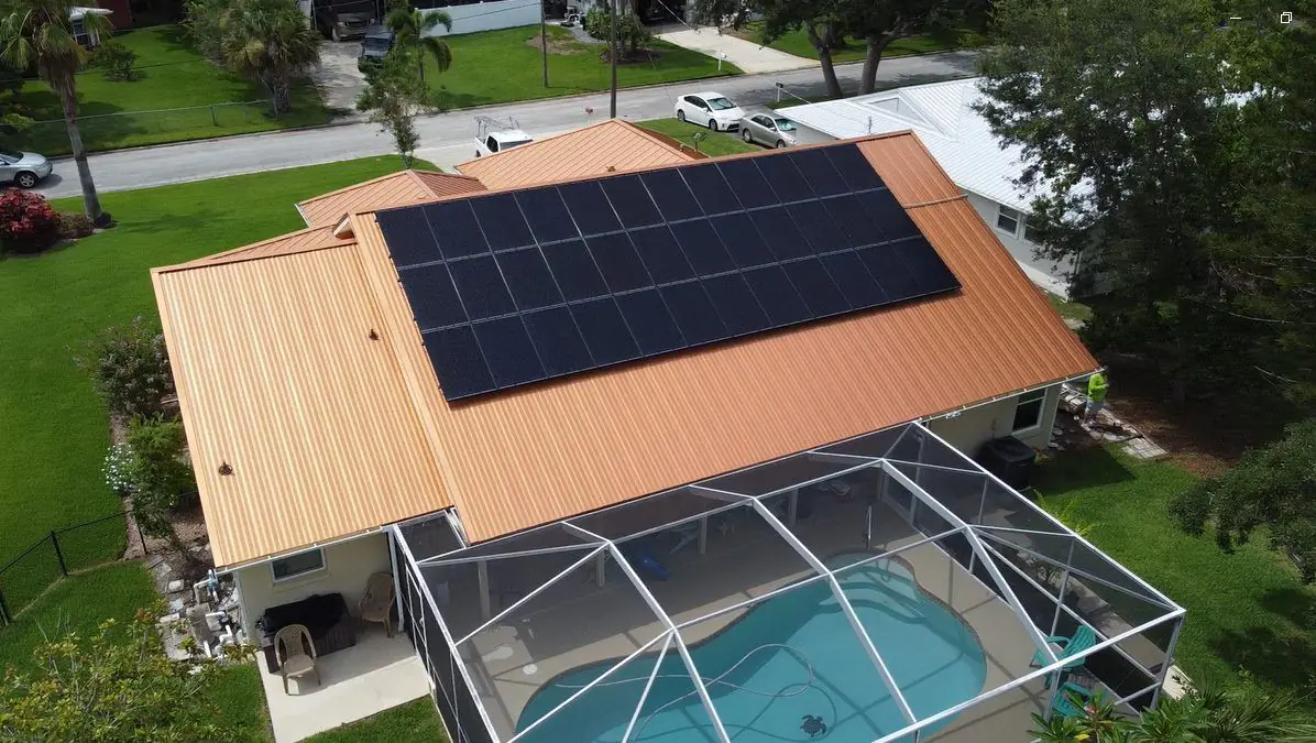 Aerial view of a home with a dark solar array on its roof beside a screened pool