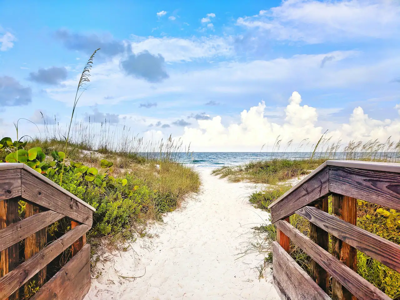 Wooden boardwalk leading over a dune to a white-sand beach