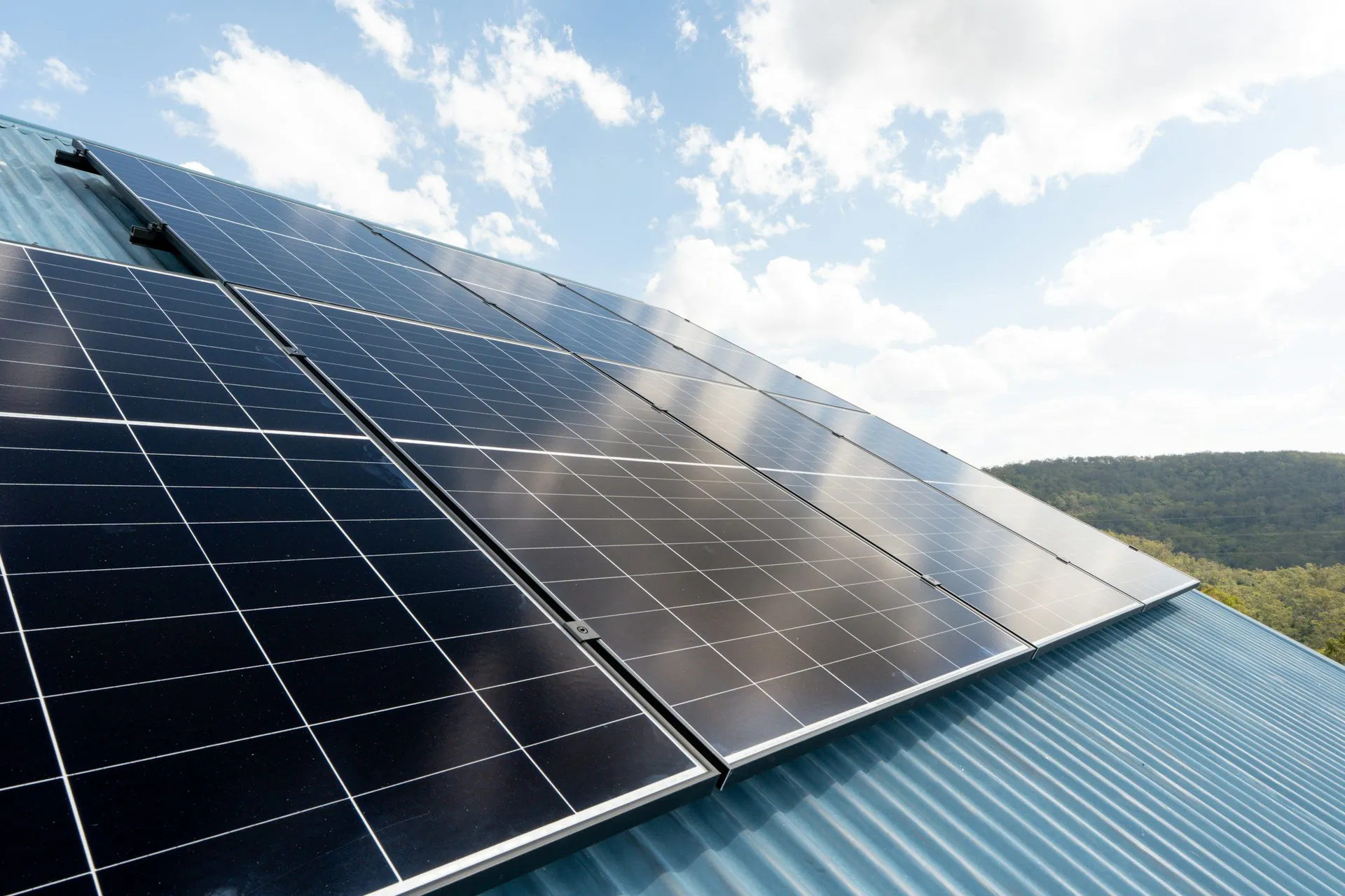 Black solar panels mounted on a ribbed teal metal roof under a bright sky