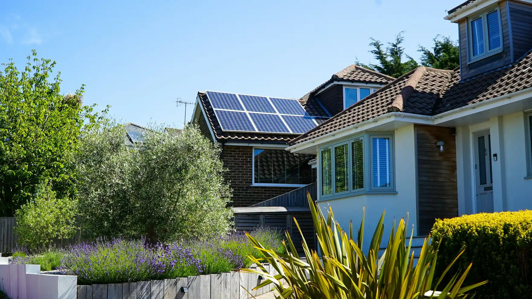 Sunny house with solar panels on its tiled roof and a planted front garden
