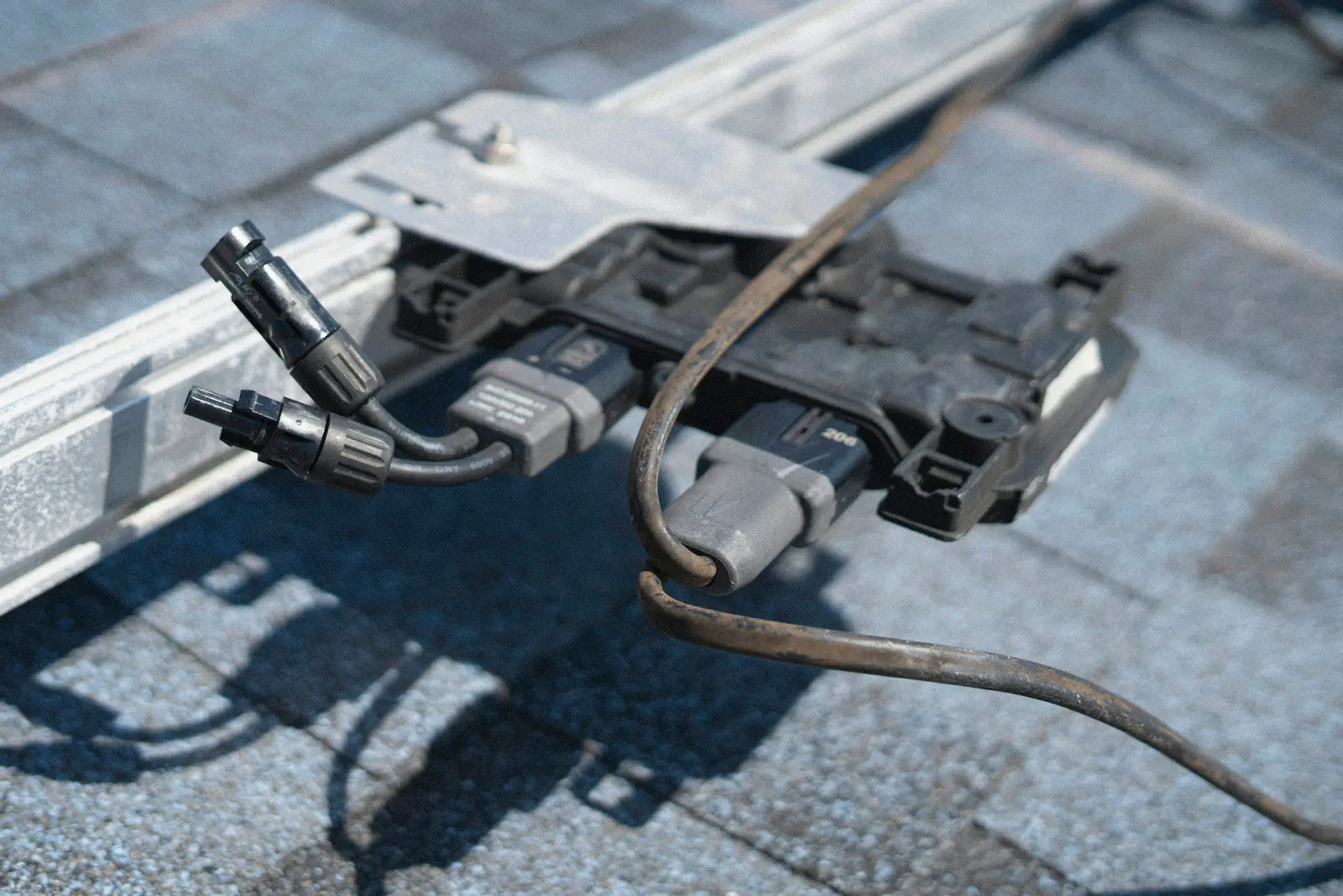 Close-up of a microinverter and cabling on solar mounting rails above a shingle roof