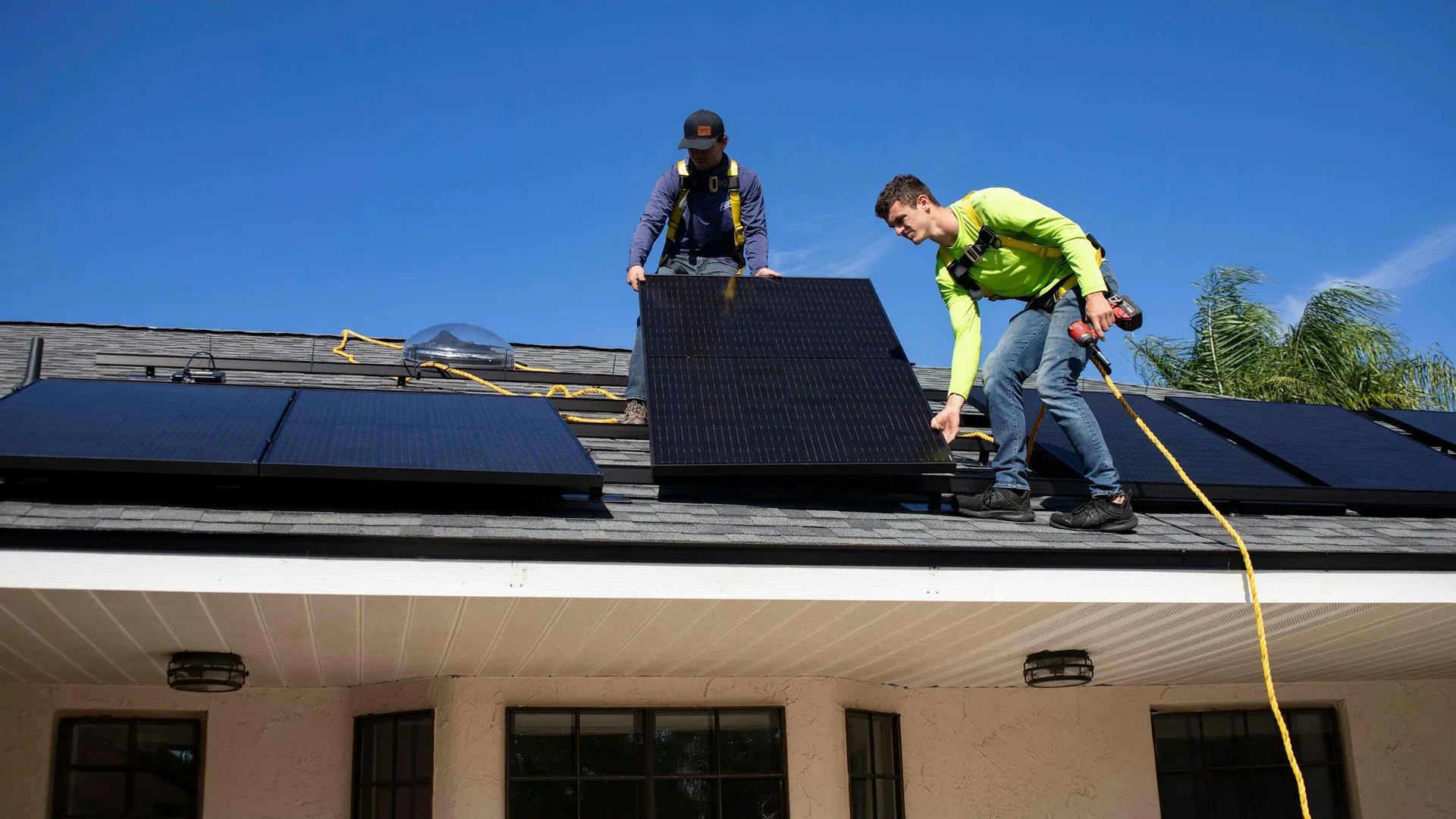 Solar installers fixing panels to the pitched roof of a house under a clear blue sky