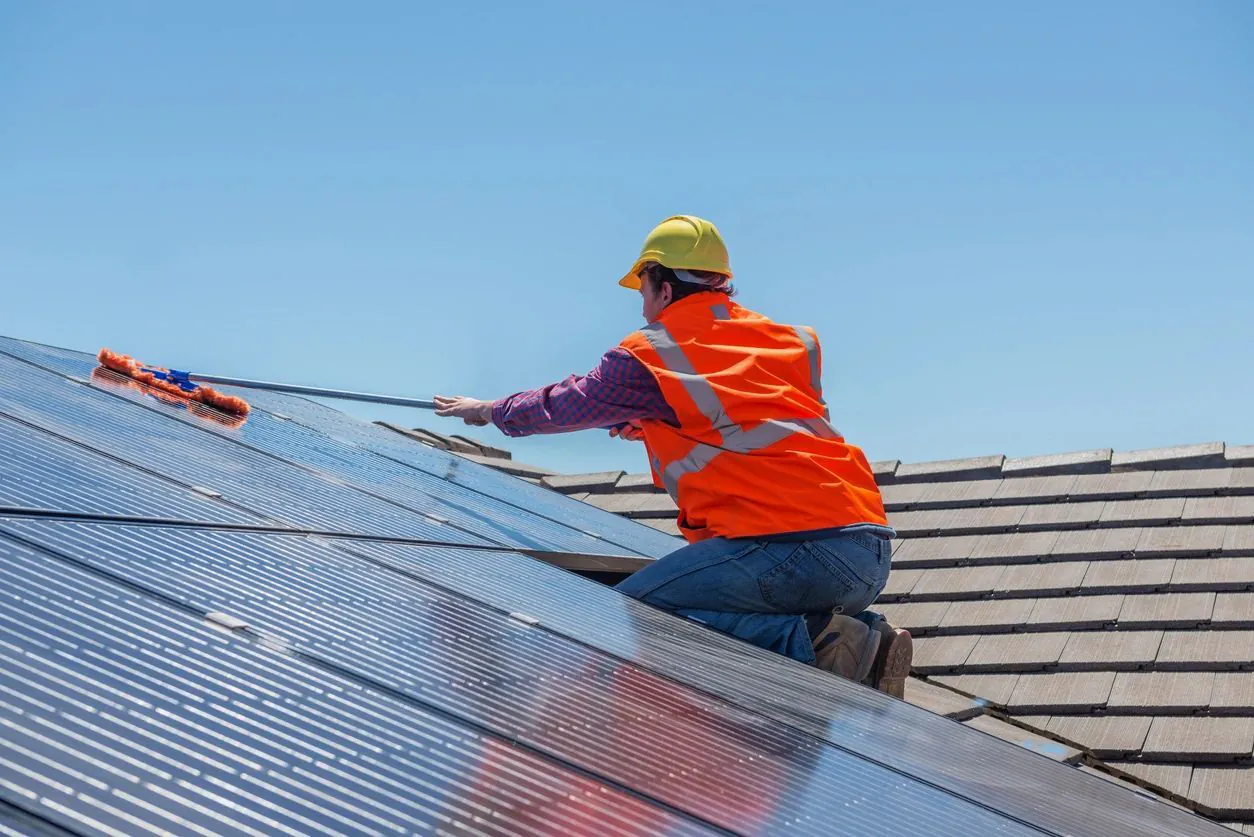 Installer in a hard hat and hi-vis vest working across solar panels on a tile roof