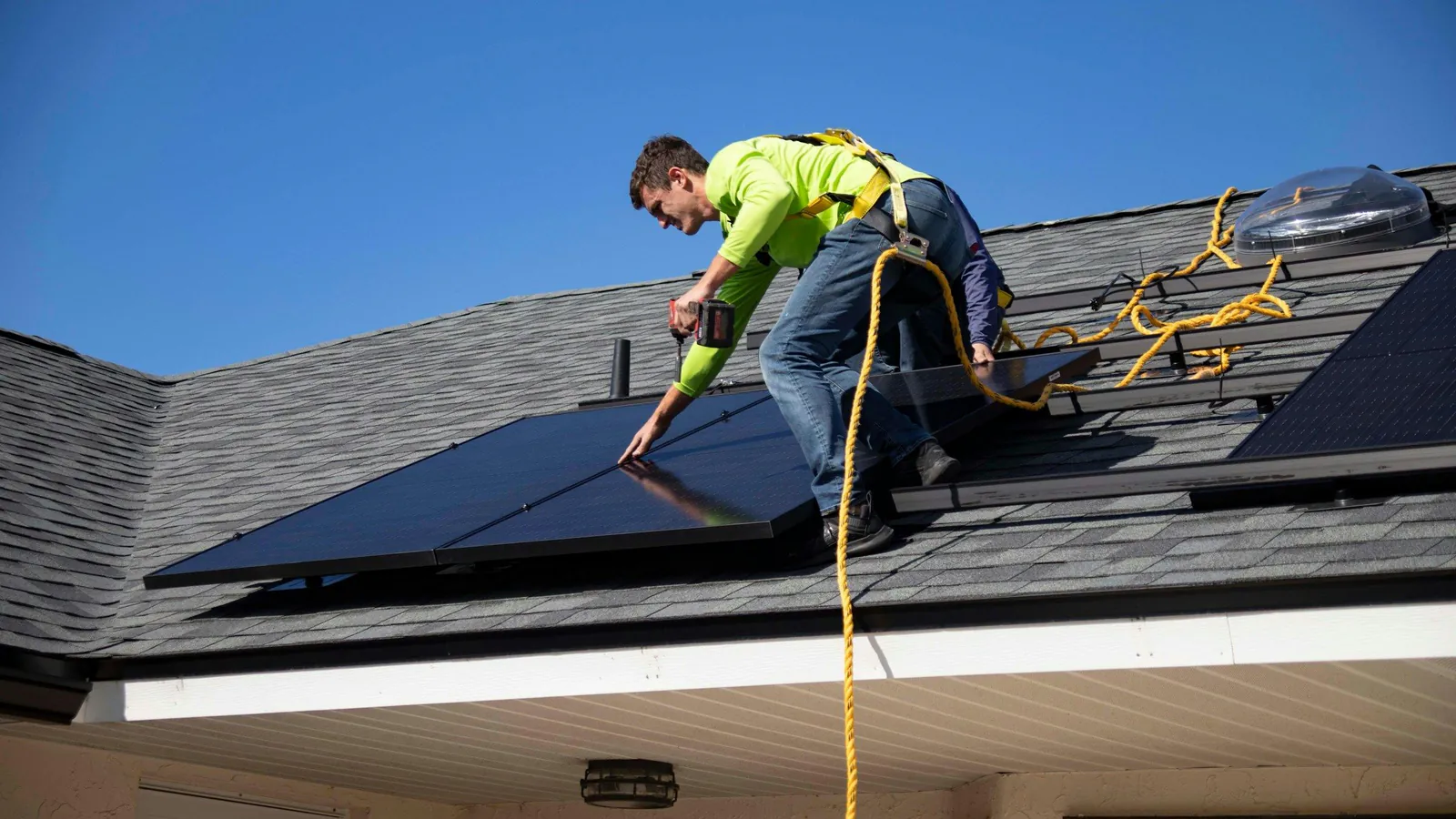Installer in hi-vis and a harness handling a solar panel on a shingle roof