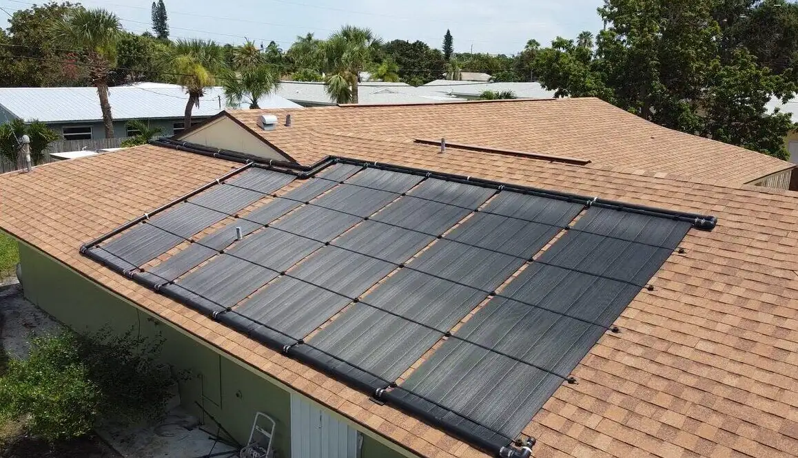 Black solar pool heating collectors laid across a terracotta shingle roof