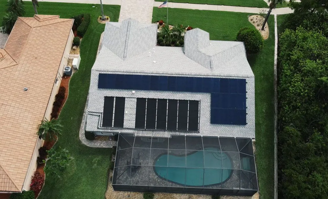 Aerial view of a solar array on a light grey roof above a screened pool enclosure