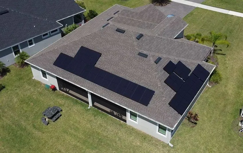 Aerial view of a solar array on a grey shingle roof with a green lawn around the house