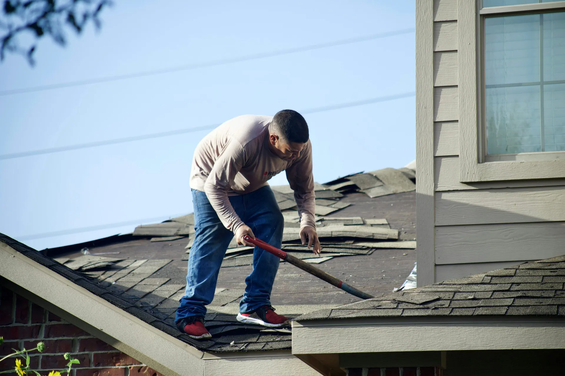 Roofer stripping old shingles from a house roof