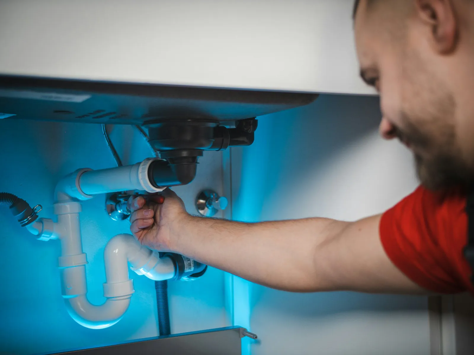 Technician adjusting shut-off valves and pipework under a unit